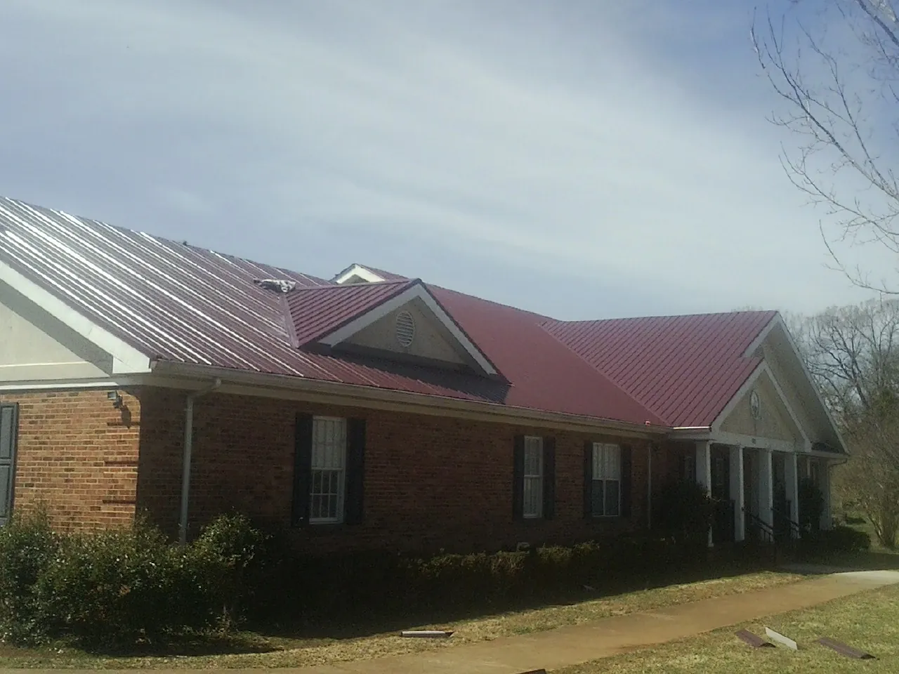 Red metal roof with gabled entries on a long brick building, from a Hail Damage Roof Repair job in Converse