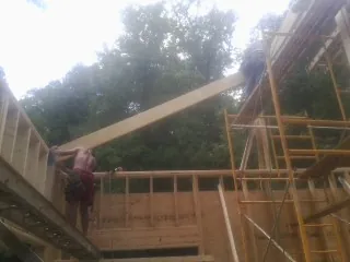 Carpenter raising a rafter beam on a new second story frame in Converse